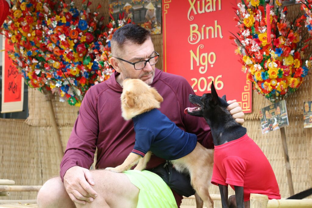 A man enjoying the Tet festival in Vietnam with his dogs. Vibrant floral decorations in the background.